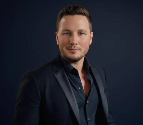 Portrait of a man in dark blazer and shirt against blue background, professional headshot style photo